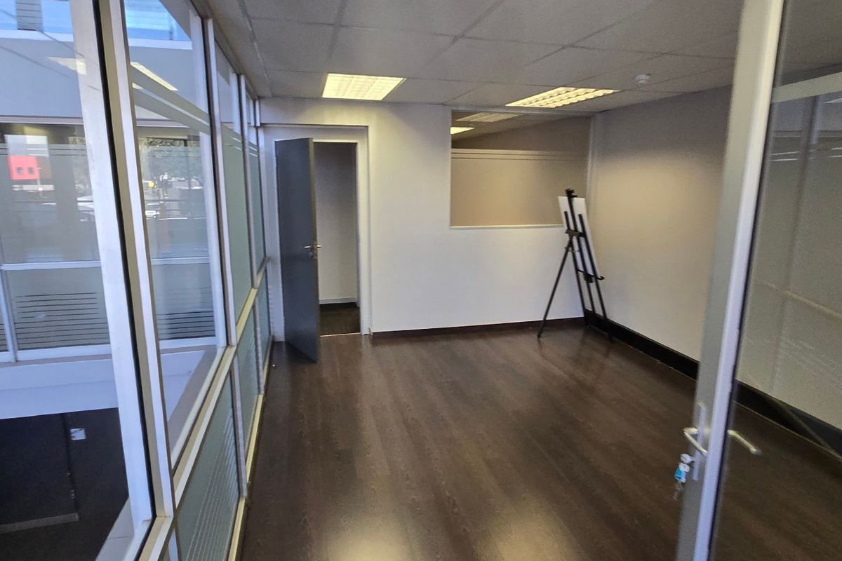 A vacant commercial office suite featuring dark laminate flooring, glass partition walls, and a suspended ceiling with recessed lighting.