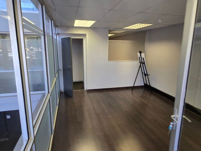 A vacant commercial office suite featuring dark laminate flooring, glass partition walls, and a suspended ceiling with recessed lighting.