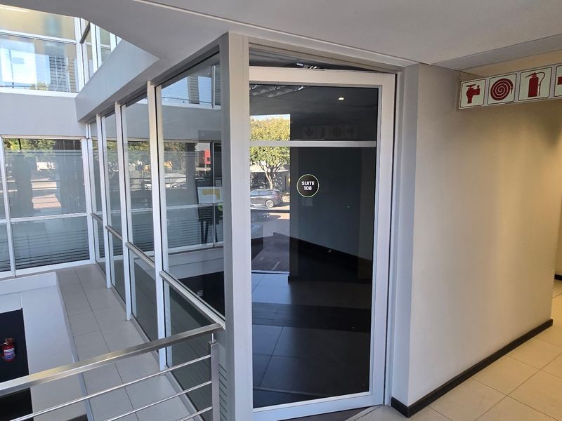 A modern commercial hallway featuring aluminium-framed glass partitioning, tiled flooring, and clear fire safety signage within a professional office building environment.