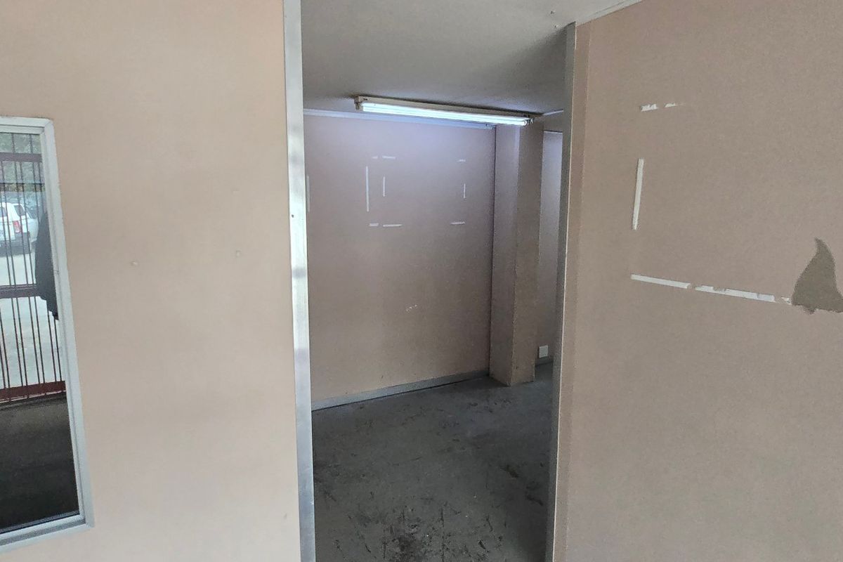 A vacant industrial hallway featuring a metal door frame, internal window, and fluorescent lighting, showing signs of wear on the walls and floor.