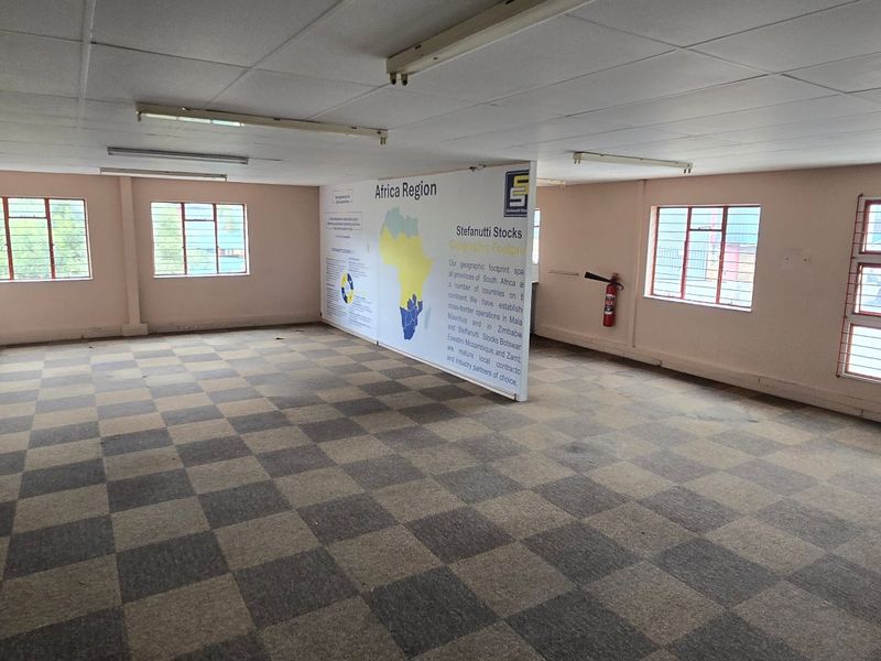 Spacious open-plan office area featuring carpet tiles, suspended ceilings, fluorescent lighting, and security bars on windows.