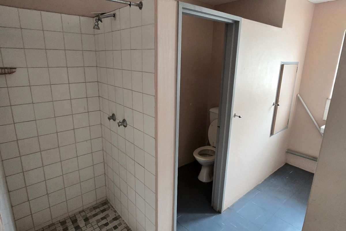 A functional bathroom featuring a tiled shower enclosure and a separate toilet area with basic finishes.
