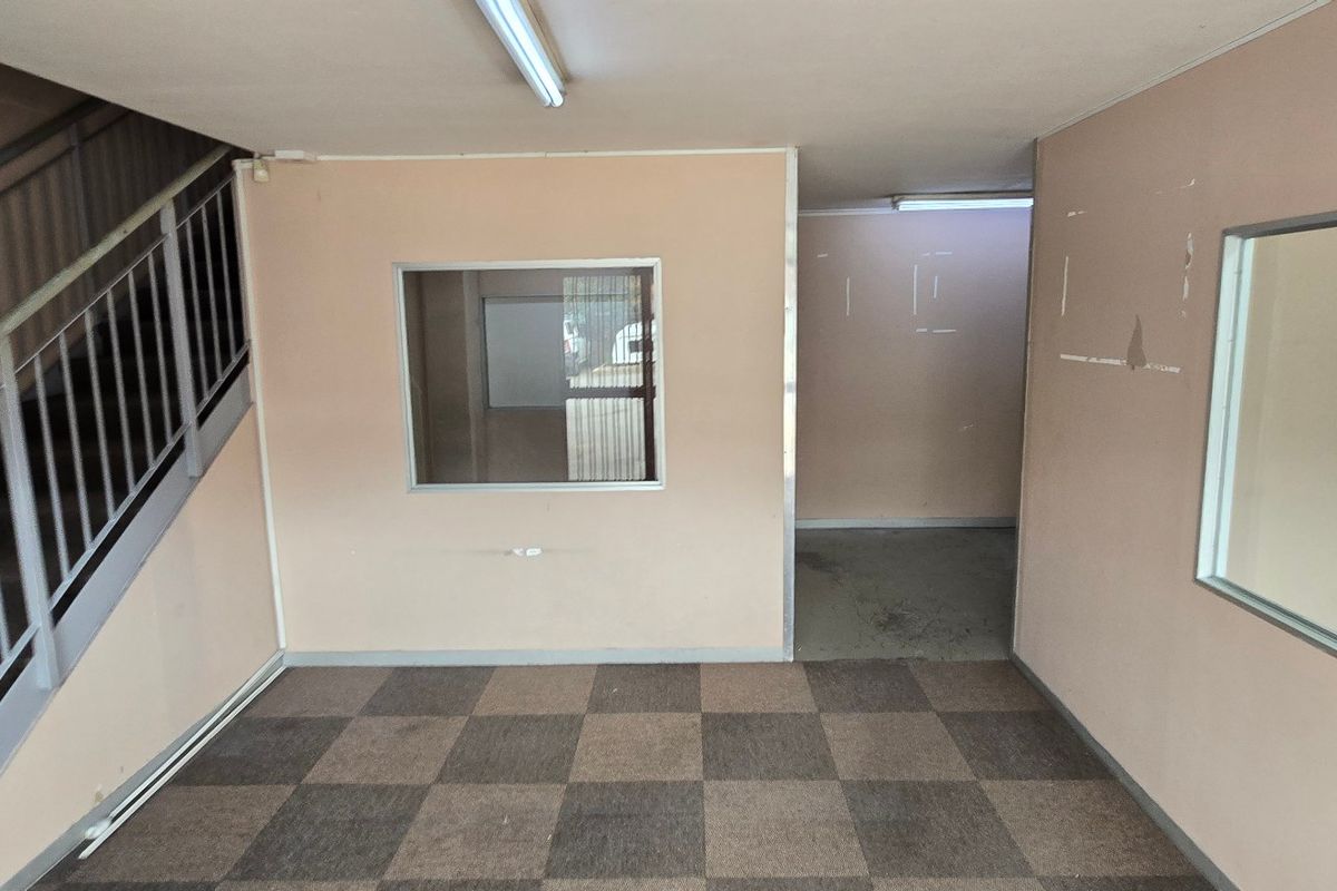An empty industrial entry area featuring carpet tiles, a metal staircase with handrails, and internal glass partitions, requiring cosmetic updates to improve the space.