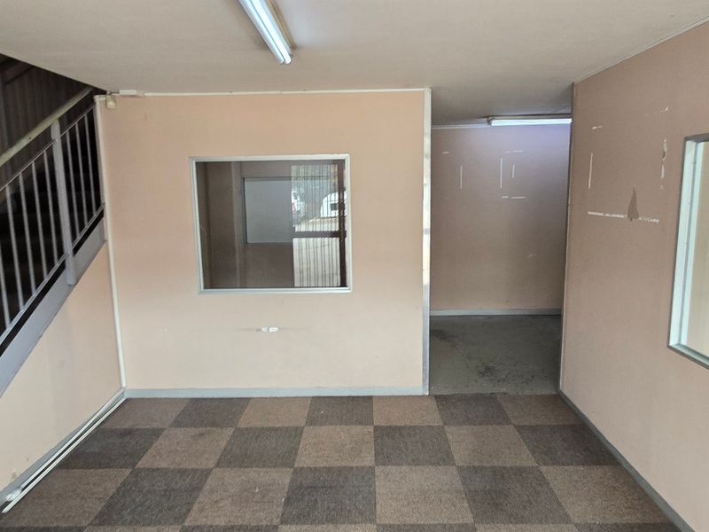 An empty industrial entry area featuring carpet tiles, a metal staircase with handrails, and internal glass partitions, requiring cosmetic updates to improve the space.