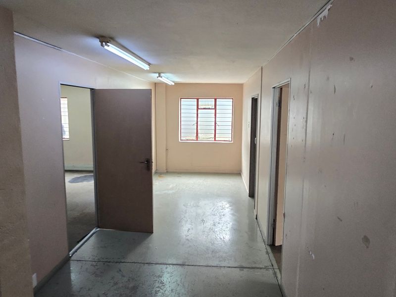 An empty industrial hallway featuring painted concrete floors, fluorescent lighting, and multiple internal access points.