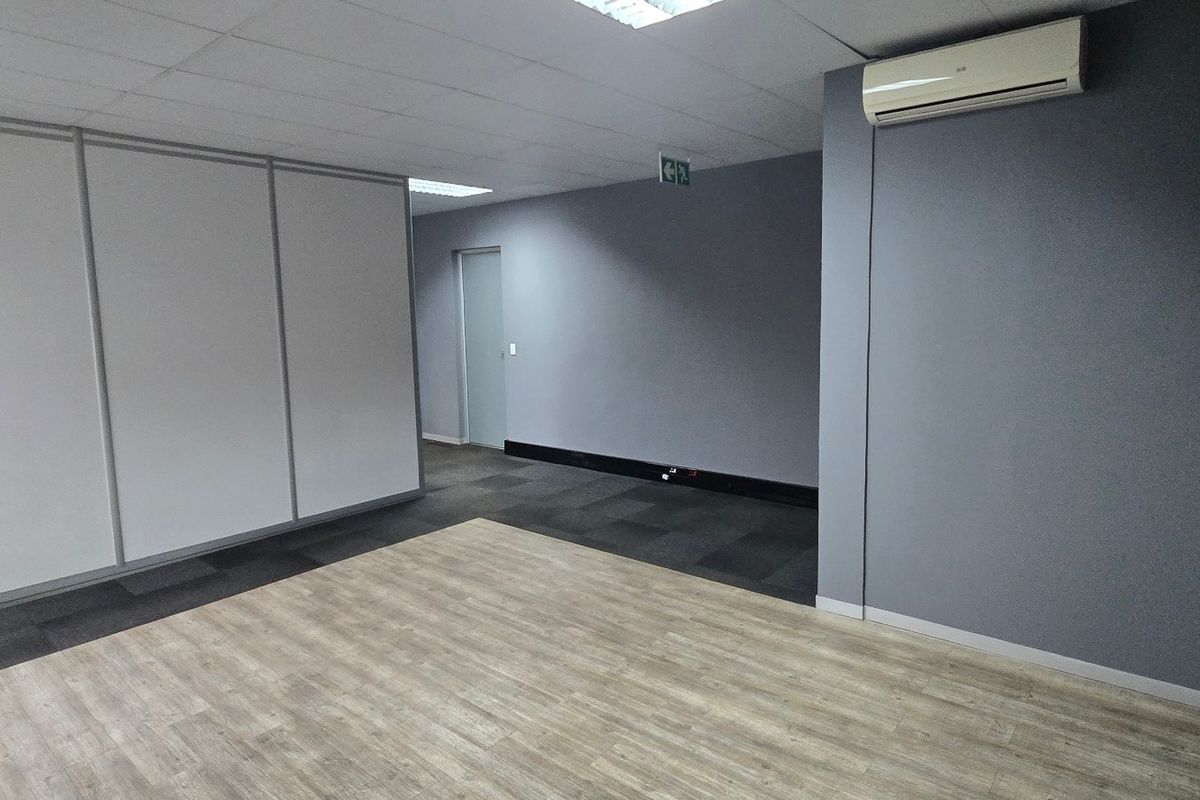 A clean, vacant commercial office space featuring a mix of laminate and carpet flooring, modular partition walls, and a wall-mounted air conditioning unit.