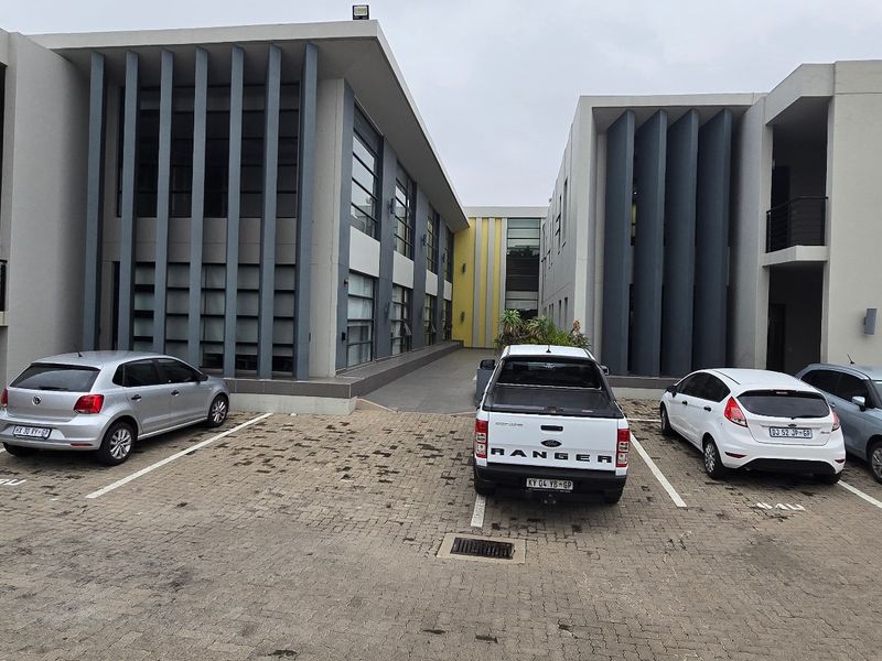 Modern commercial office complex featuring a paved parking area, contemporary architectural design with vertical fins, and multi-level building access.