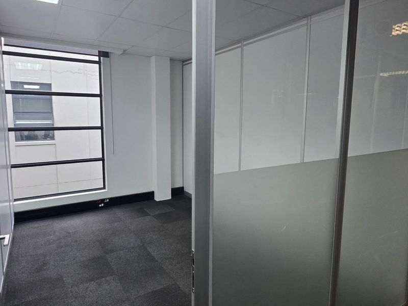 A vacant commercial office space featuring modern glass partitions, carpeted flooring, and a suspended ceiling with integrated lighting.