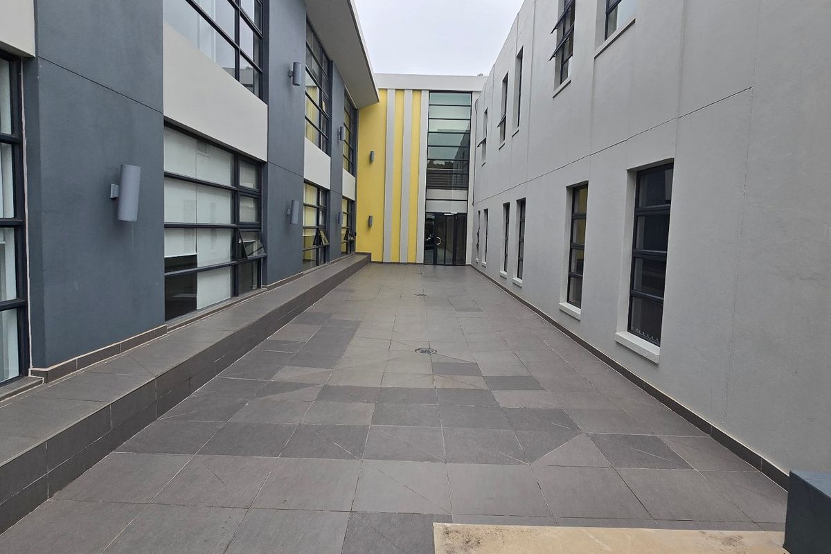 A modern commercial courtyard featuring tiled flooring and multi-story building facades with large aluminium-framed windows.