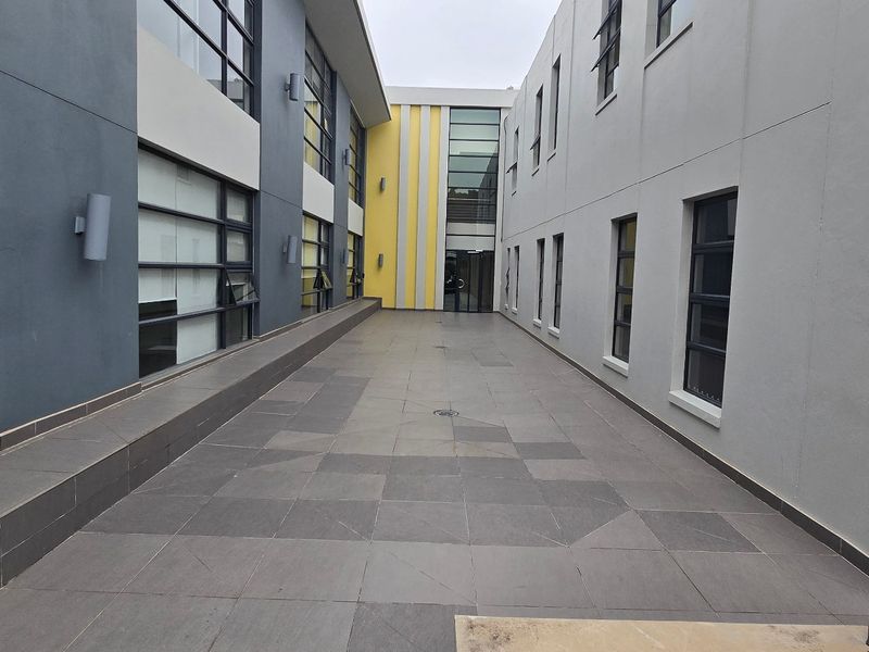 A modern commercial courtyard featuring tiled flooring and multi-story building facades with large aluminium-framed windows.