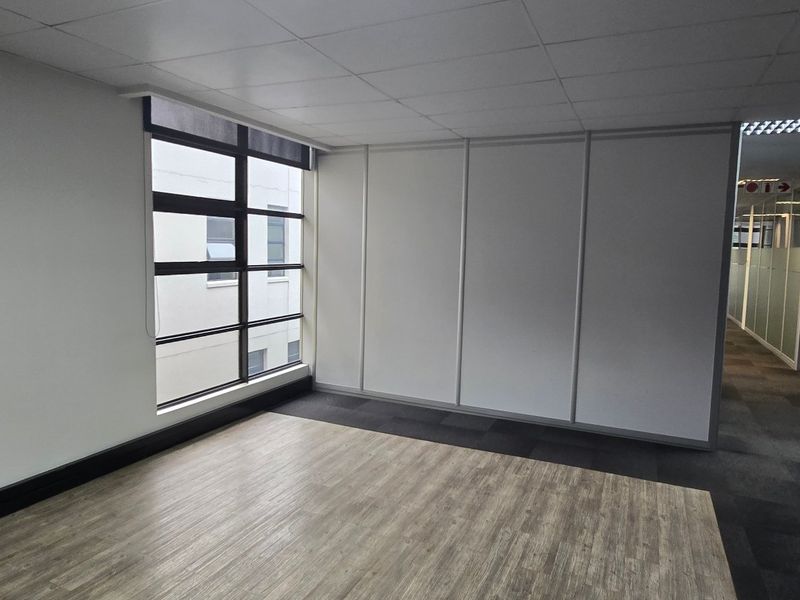 A bright, vacant office space featuring a mix of wood-look vinyl and carpet flooring, large windows, and modern partition walls.