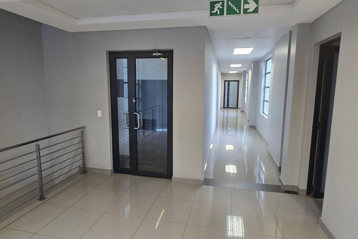 A clean, modern commercial hallway featuring polished tiled floors, recessed lighting, and glass-panelled doors with a metal balustrade.