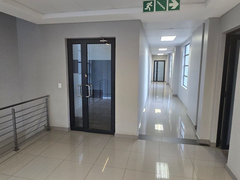 A clean, modern commercial hallway featuring polished tiled floors, recessed lighting, and glass-panelled doors with a metal balustrade.