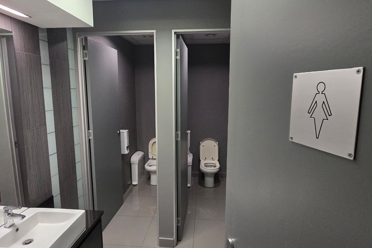 Modern commercial female restroom featuring dual toilet cubicles, a vanity basin with mixer tap, and contemporary tiled finishes.