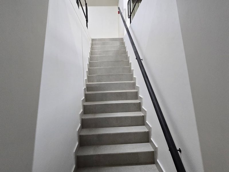 A clean, modern staircase featuring concrete steps and a minimalist black metal handrail, providing access between levels in an industrial-style property.