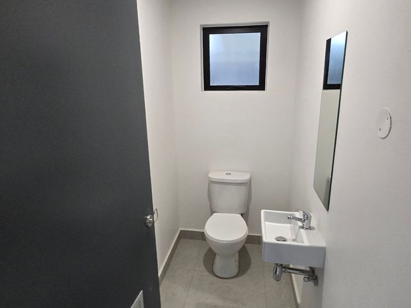 A clean, modern guest bathroom featuring a white toilet, wall-mounted basin with chrome faucet, and neutral tiled flooring.