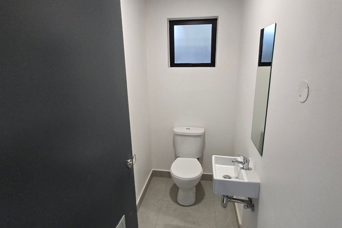 A clean, modern guest bathroom featuring a white toilet, wall-mounted basin with chrome faucet, and neutral tiled flooring.