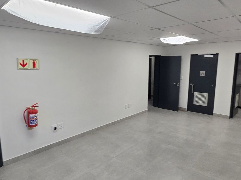 A clean, modern office space featuring tiled flooring, recessed lighting, and a small kitchenette area, suitable for professional use.