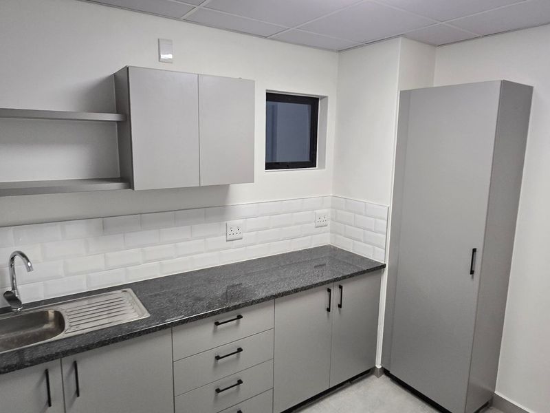 A clean, modern kitchenette featuring grey built-in cabinetry, granite countertops, a stainless steel sink, and a classic white subway tile backsplash.