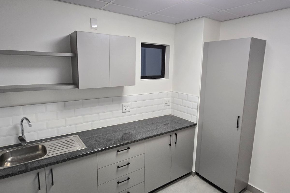 A clean, modern kitchenette featuring grey built-in cabinetry, granite countertops, a stainless steel sink, and a classic white subway tile backsplash.