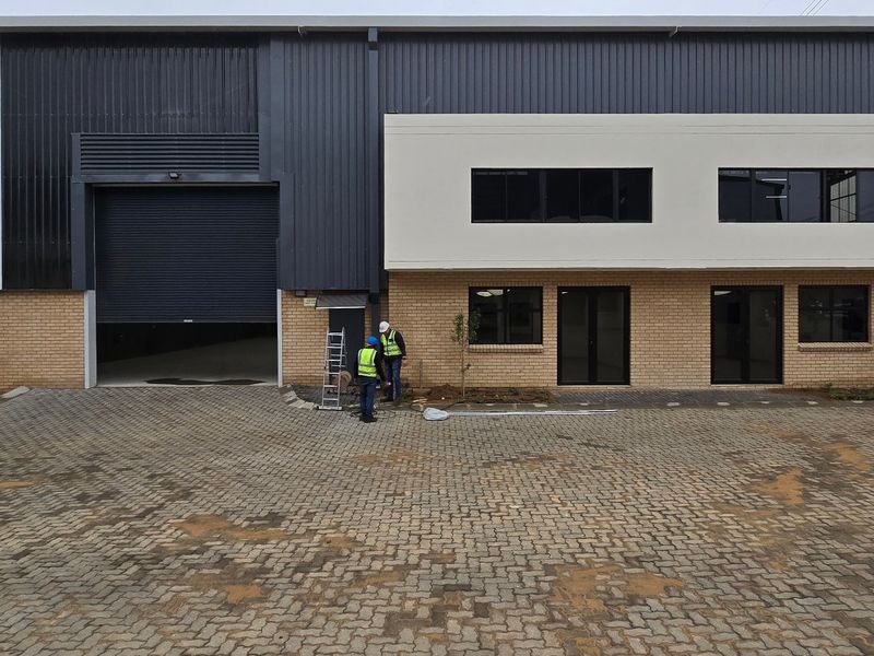 Modern industrial warehouse unit featuring a large roller shutter door, brick and metal cladding facade, and paved driveway access.