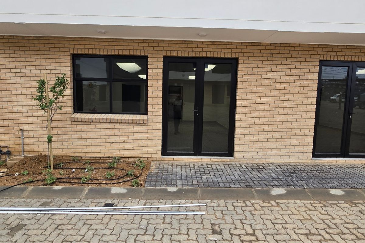 Front elevation of an industrial property featuring face brick facade, black aluminium framed windows and double doors, with paved access and integrated lighting.