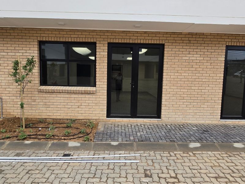 Front elevation of an industrial property featuring face brick facade, black aluminium framed windows and double doors, with paved access and integrated lighting.
