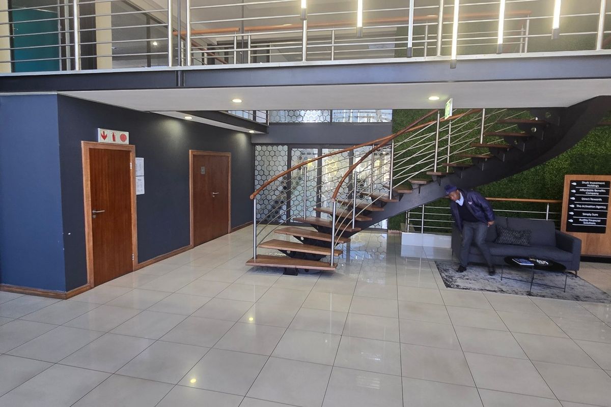 Modern commercial entrance lobby featuring a striking open-tread staircase, mezzanine level, tiled flooring, and contemporary finishes.