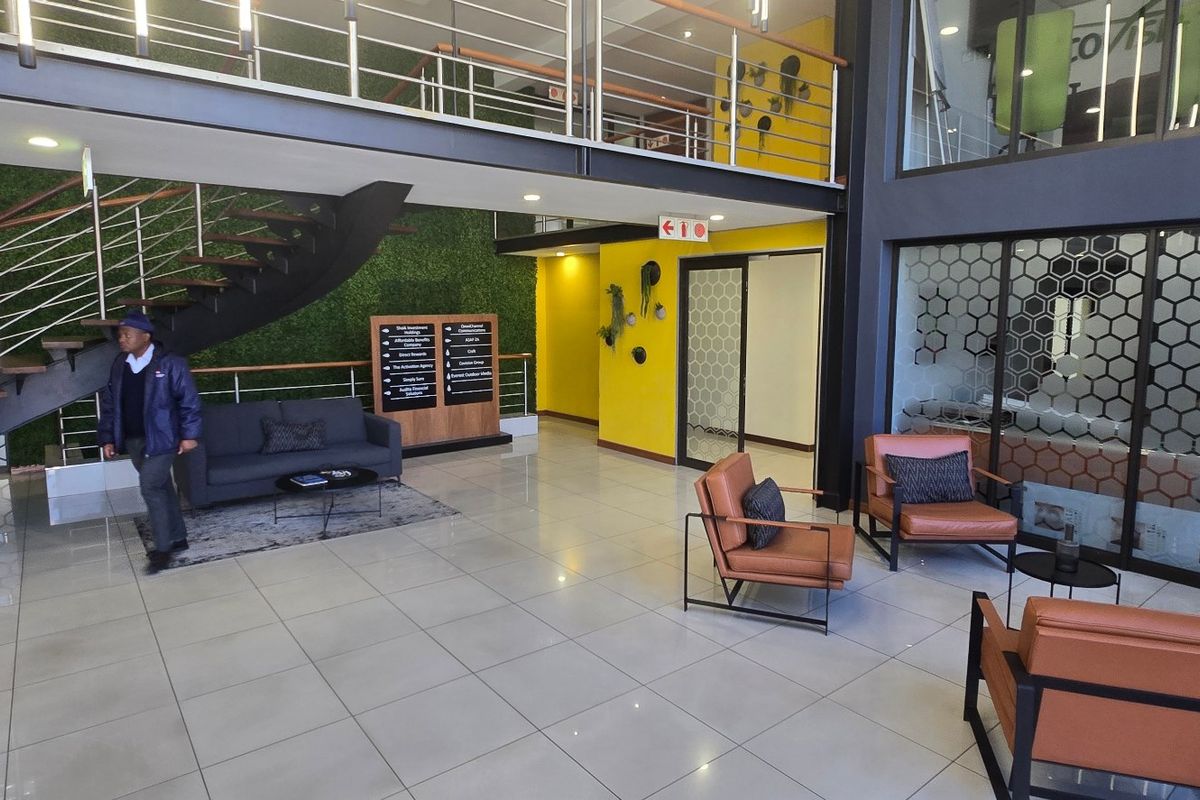 Modern commercial entrance lobby featuring a floating staircase, mezzanine level, glass partitions, and contemporary tiled flooring with high ceilings.