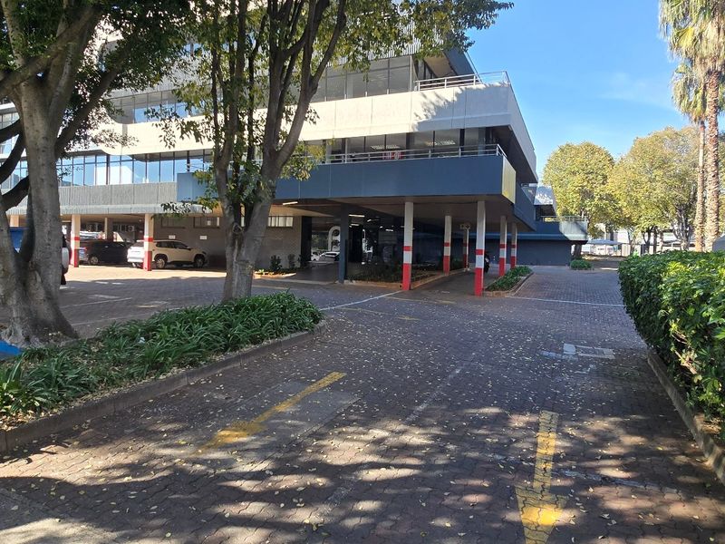 Exterior view of a commercial office building featuring a paved driveway, covered parking bays, and established landscaping.