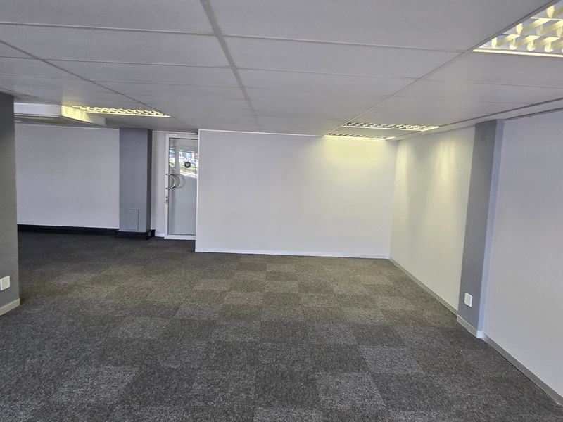 A spacious, open-plan commercial office area featuring neutral finishes, carpeted flooring, recessed lighting, and a clean, professional aesthetic suitable for various business configurations.