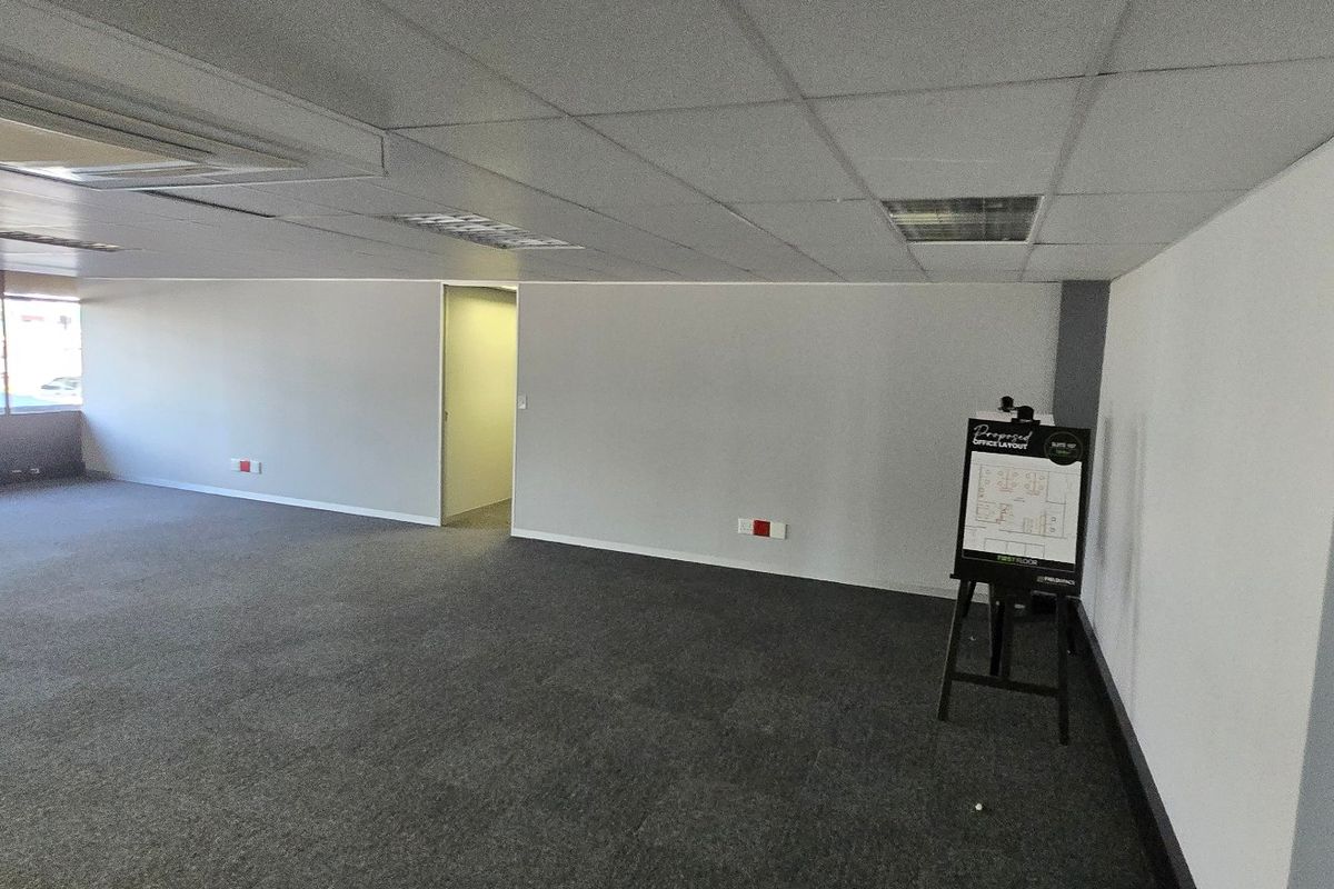 A spacious, open-plan commercial office area featuring neutral carpeting, a suspended ceiling with recessed lighting, and integrated ducted air conditioning.