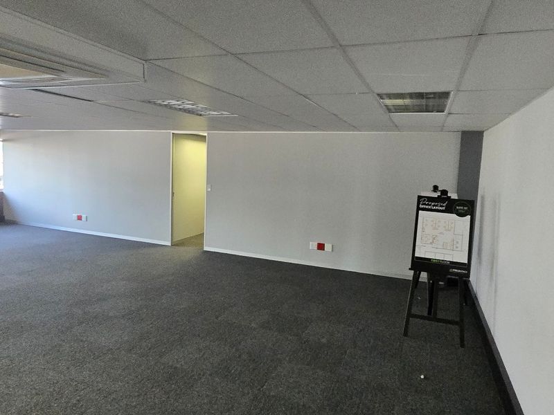 A spacious, open-plan commercial office area featuring neutral carpeting, a suspended ceiling with recessed lighting, and integrated ducted air conditioning.