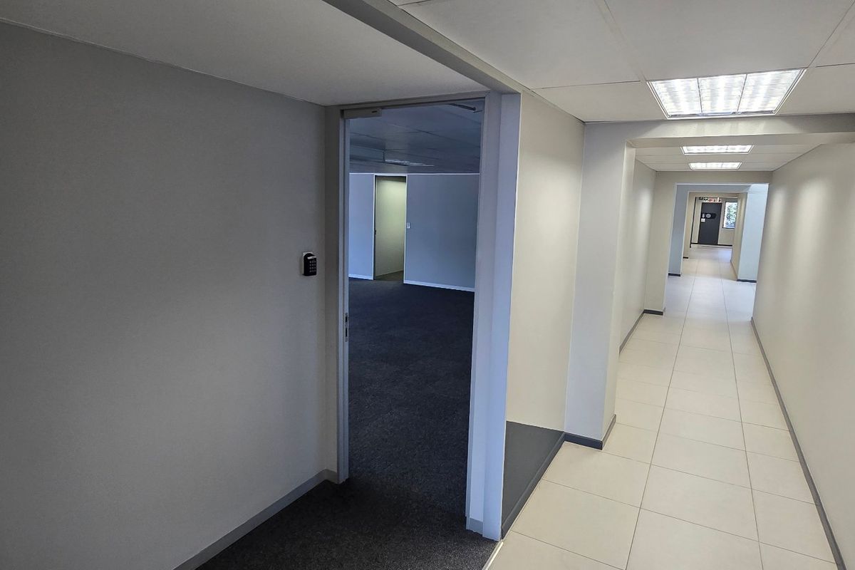 A clean, modern commercial hallway featuring neutral walls, tiled flooring, recessed lighting, and a secure keypad entry system leading into an office space.