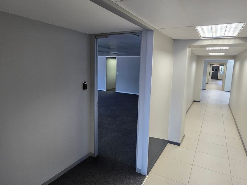 A clean, modern commercial hallway featuring neutral walls, tiled flooring, recessed lighting, and a secure keypad entry system leading into an office space.