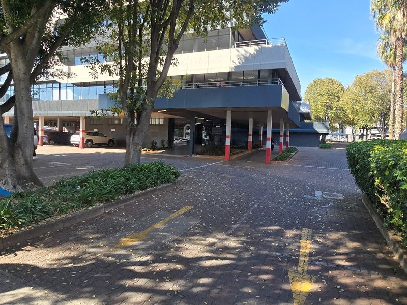 Exterior view of a commercial office building featuring a paved driveway, covered parking bays, and established landscaping.