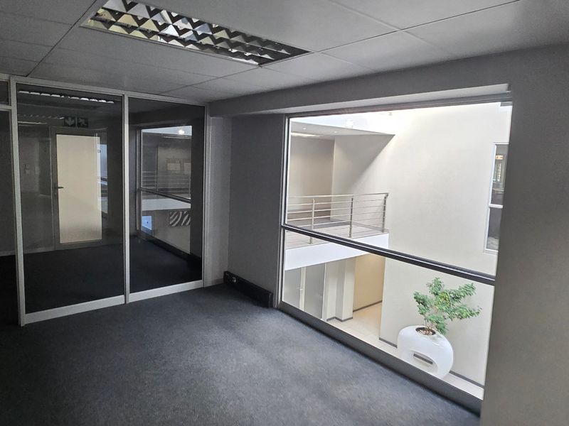 A vacant commercial office space featuring carpeted flooring, suspended ceilings with recessed lighting, and glass partitions overlooking an internal atrium.