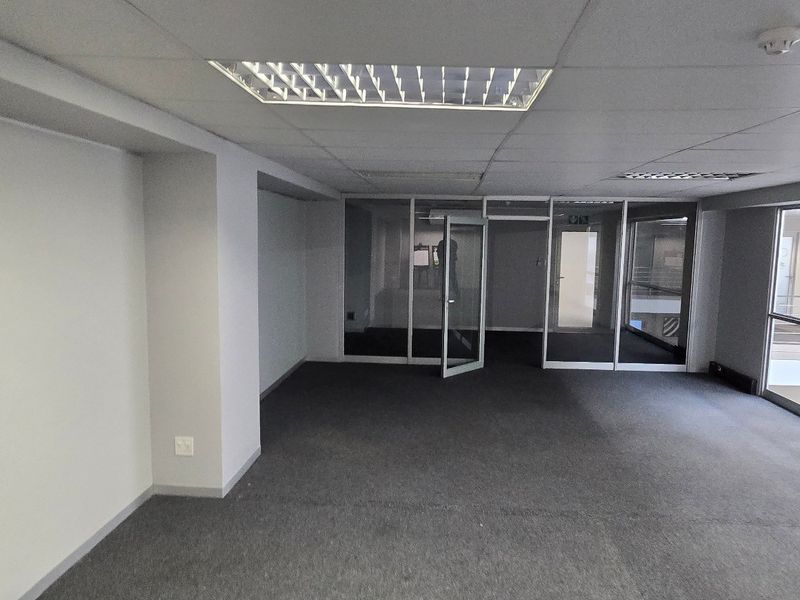 A vacant commercial office space featuring glass partitions, suspended ceilings with recessed lighting, and carpeted flooring, offering a clean and professional work environment.