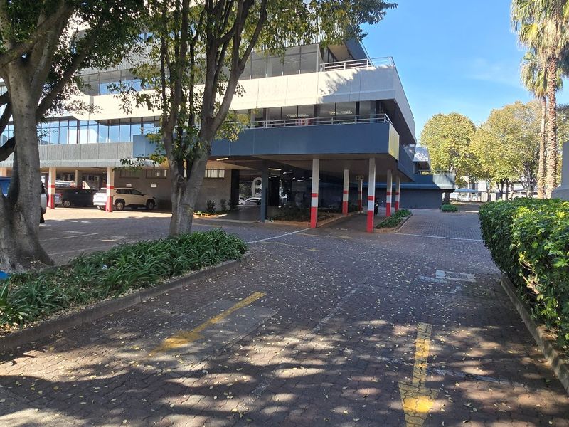 Exterior view of a commercial office building featuring a paved driveway, covered parking bays, and established landscaping.