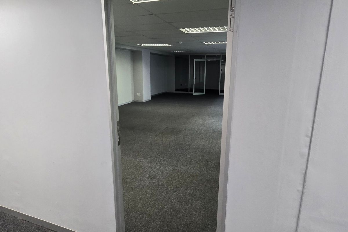 A vacant commercial office space featuring neutral carpet flooring, a suspended ceiling with recessed lighting, and a glass partition door.
