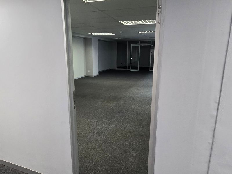 A vacant commercial office space featuring neutral carpet flooring, a suspended ceiling with recessed lighting, and a glass partition door.
