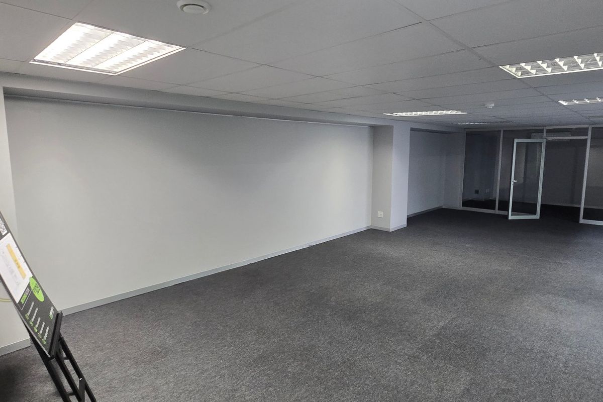 A spacious, empty commercial office area featuring a suspended ceiling, recessed lighting, carpeted floors, and glass partition walls for a modern, professional workspace.