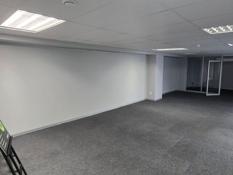 A spacious, empty commercial office area featuring a suspended ceiling, recessed lighting, carpeted floors, and glass partition walls for a modern, professional workspace.