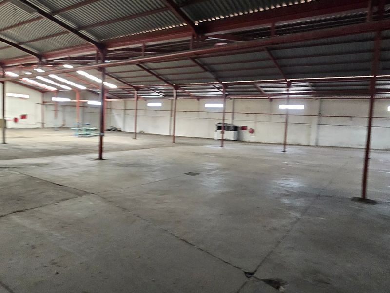 A large, open-plan industrial warehouse space featuring concrete flooring, a steel portal frame structure, and high-level clerestory windows for natural light.