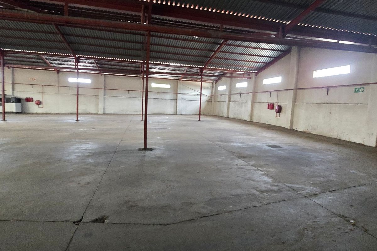 Spacious industrial warehouse featuring high ceilings with exposed steel trusses, concrete flooring, and integrated fire safety equipment.