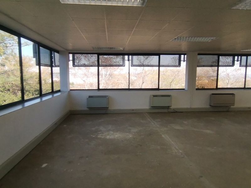 An empty, open-plan commercial office space featuring large windows, wall-mounted air conditioning units, and a suspended ceiling with recessed lighting.