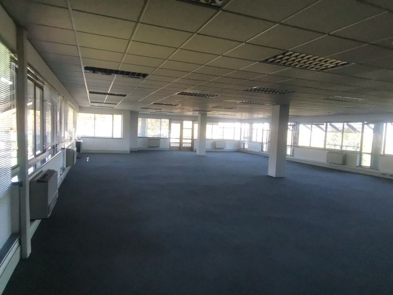 A spacious, open-plan commercial office area featuring large windows, suspended ceilings, and wall-mounted HVAC units, offering a versatile workspace layout.