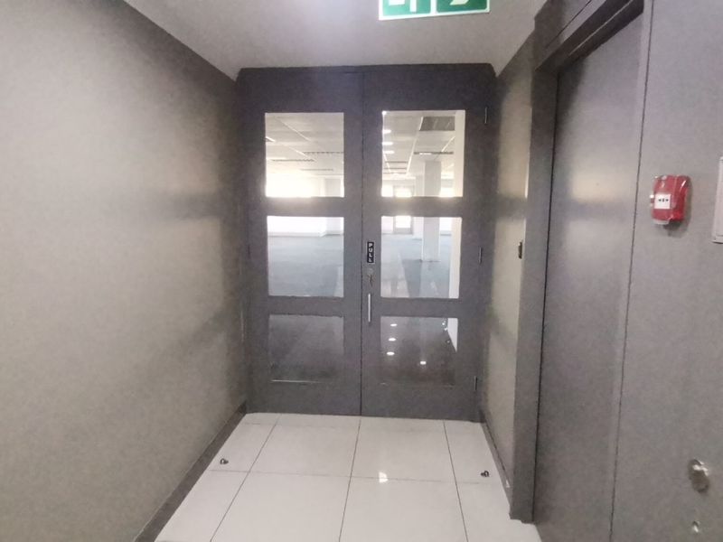 A clean commercial entry foyer featuring double glass doors, tiled flooring, and integrated fire safety equipment, leading into an open-plan office space.