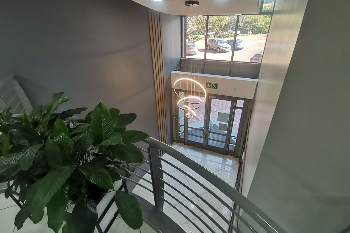 Modern commercial entrance foyer featuring high ceilings, large glass doors, polished tile flooring, and a contemporary spiral pendant light fixture.