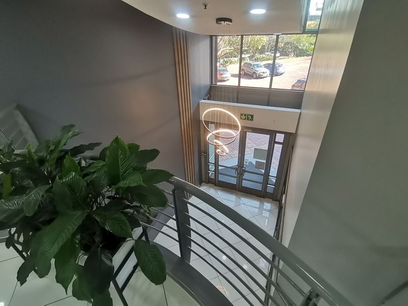 Modern commercial entrance foyer featuring high ceilings, large glass doors, polished tile flooring, and a contemporary spiral pendant light fixture.